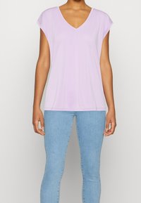 Lila kortärmad V-ringad topp i ett mjukt tyg, tillsammans med ljusblå skinny jeans. Toppen har en avslappnad passform och korta ärmar.