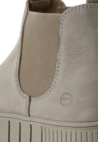 Beige leren enkelboot met elastische zijkanten, contrasterende stiksels en een gestructureerde rubberen zool. Bevat een gegraveerd logo detail.