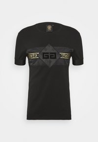 Schwarzes T-Shirt mit einem glänzenden, schwarzen, diamantförmigen Patch mit Prägung des Logos, akzentuiert durch ein goldenes geometrisches Band über der Brust.