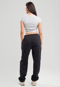 Harmaa lyhythihainen t-paita, joka on lyhennetty, yhdistetty mustiin collegehousuihin, joissa on joustava vyötärö ja takatasku, nähtynä takaa.