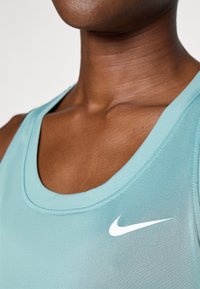 Een lichtblauw sporttanktop met een ronde hals, gemaakt van soepel materiaal, heeft een wit Nike-logo aan de linkerkant.