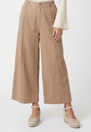 Beige weit geschnittene, gekürzte Hose, getragen mit hellbeigen Keilabsatz-Espadrilles und einem cremefarbenen Langarmoberteil, von der Taille bis zu den Füßen gezeigt.