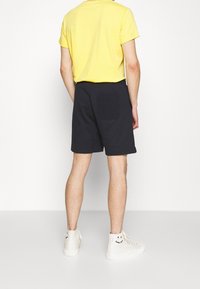 T-shirt en coton jaune à manches courtes, associé à un short bleu marine avec une poche arrière. Porté avec des baskets blanches montantes.