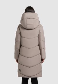 Heledad mantel heled bees värviga, paksu vööndiga disainiga, suure kapuutsiga ja nähtava brändi logoga alumisel äärel. Sile tekstuur ja polsterdatud viimistlus.