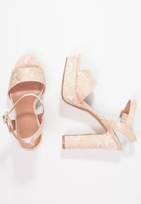 Pair of pink and gold brocade open-toe block heel sandals with ankle straps on a white background.