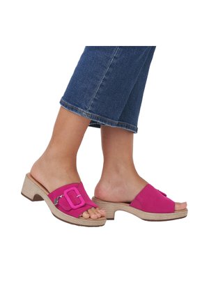 Des pieds portant des sandales à talons blocs ouvertes rose avec une boucle décorative, associées à un jean denim bleu cropped sur fond blanc.