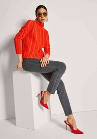 Roter strukturierter Pullover mit hohem Kragen, kombiniert mit dunklen Skinny Jeans und roten Slingback-Heels mit spitzer Zehenpartie und Stiletto-Absatz.