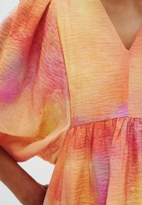 Abito leggero e multicolore con scollatura a V, maniche a palloncino e vita arricciata. Il tessuto presenta una sfumatura di arancione, rosa e giallo.