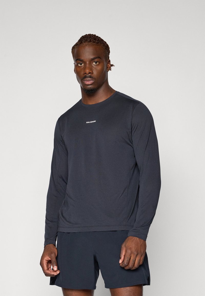 Dunkles, langärmliges Sportshirt aus leichtem Stoff, mit Rundhalsausschnitt und dem Logo "SALOMON" in Weiß auf der Brust.