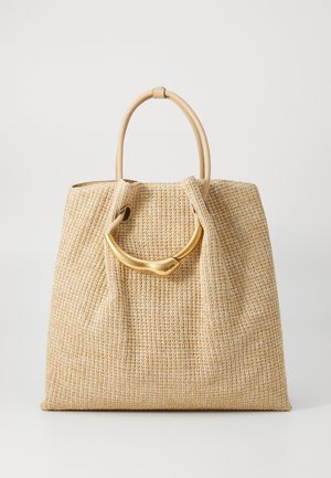 Sac fourre-tout tissé beige avec une poignée dorée proéminente, placé sur un fond blanc uni. Le sac semble spacieux et élégant.