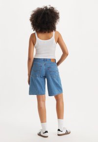 Modre jeans kratke hlače z ohlapnim krojem, petimi žepi in značilnim šivom na zadnji strani. Oblečene z belo majico brez rokavov in supergami.