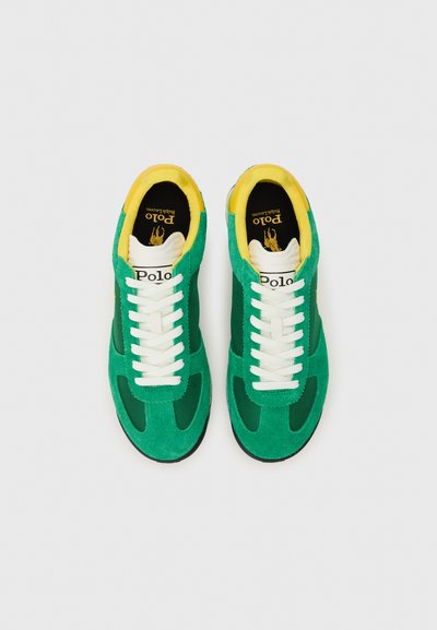 Zelené semišové tenisky s bielymi šnúrkami, žltým lemovaním a sieťovinovými panelmi. Obsahujú nášivku s logom na jazyku a gumovú podrážku.