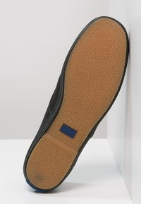 Musta kangastennari, jossa on kuvioitu kumipohja, sininen logo sivussa ja sileä, pyöreä kärki.