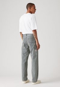 Pantalones a rayas gris y blanco con un ajuste relajado, que cuentan con bolsillos laterales y una etiqueta de parche en la parte posterior, combinados con una camiseta blanca.