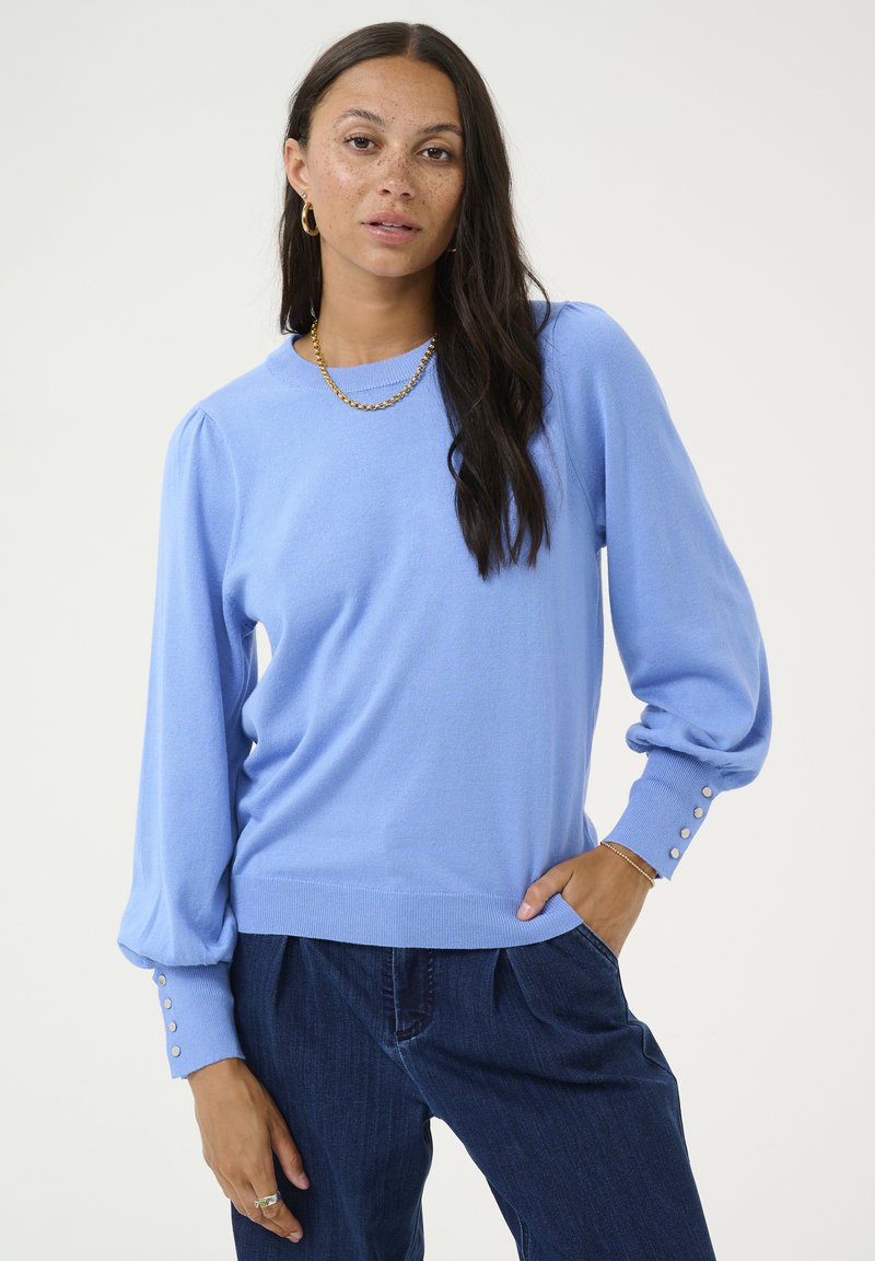 Pull en maille bleu avec un col rond, des manches bouffantes et des boutons décoratifs aux poignets. Texture douce et coupe décontractée.