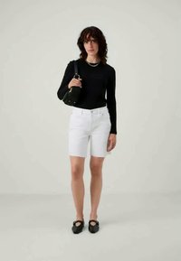 Hvit denimshorts med en tettsittende design, kombinert med en svart langermet topp og svart veske, med en glat overflate og klassisk snitt.