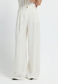 Wijd uitgesneden broek in witte stof, met een hoge taille, geplooide voorkant en een gouden knoopsluiting. Glad textuur met een getailleerde pasvorm.