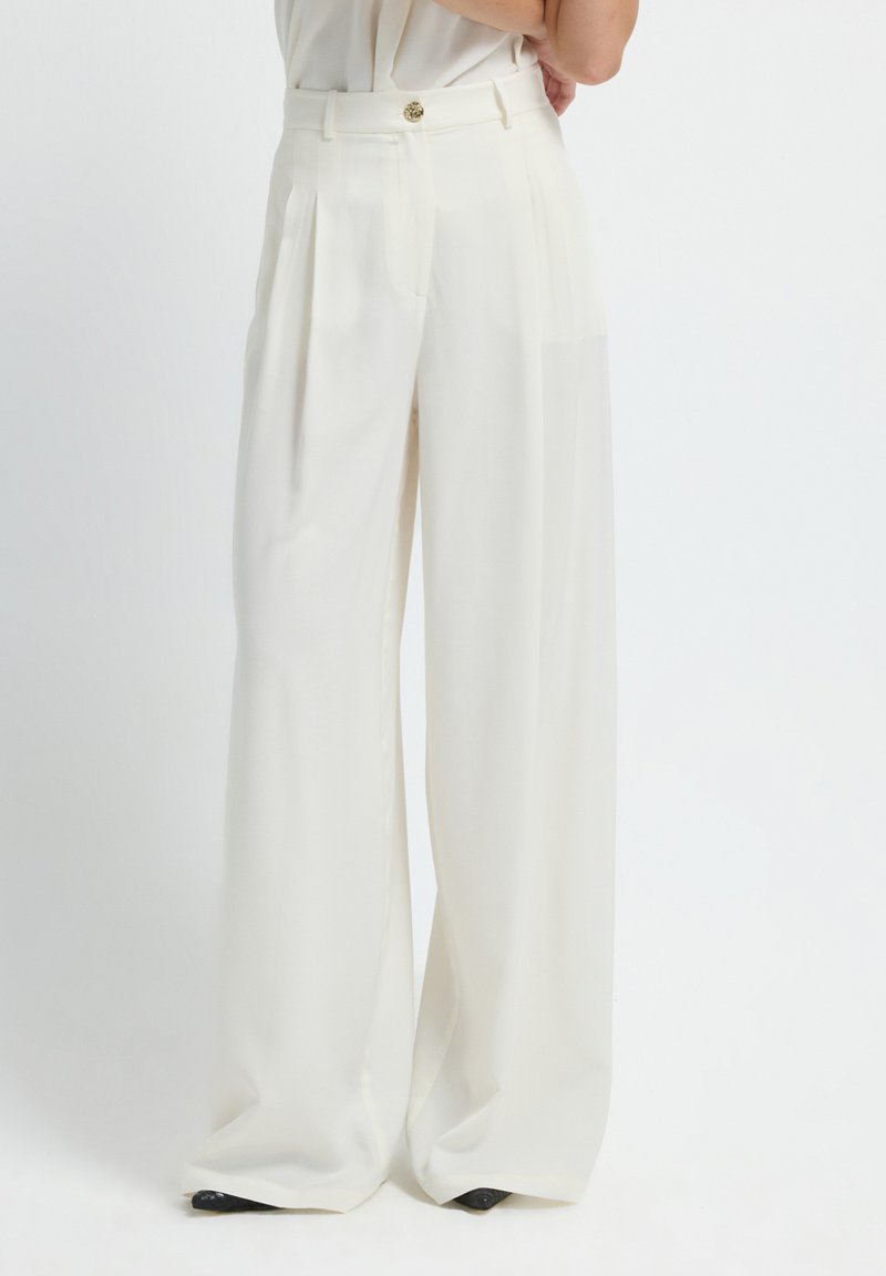 Wijd uitgesneden broek in witte stof, met een hoge taille, geplooide voorkant en een gouden knoopsluiting. Glad textuur met een getailleerde pasvorm.