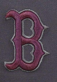 Lila gestickter Buchstabe "B" auf einem grauen strukturierten Stoffhintergrund, umrandet von grauem Stich, mit einem kunstvollen Design und spitzen Akzenten.