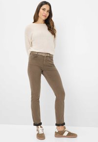 Maglione beige chiaro, pantaloni slim-fit marroni con cintura, in evidenza una fibbia della cintura. Sneakers marroni con accenti bianchi, risvolti sui pantaloni.