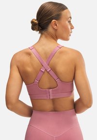 Sostén deportivo rosa con tirantes cruzados y cierre de gancho ajustable. Textura suave con un diseño ajustado, combinado con leggings de cintura alta a juego.