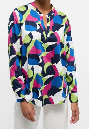 Overhemd met lange mouwen met blauwe, roze, groene, marineblauwe en witte abstracte vormen, gedragen met een witte broek, vooraan met een ingesneden kraag.