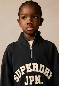 Svart zip-up sweatshirt med hög krage, med krämfärgad text "SUPERDAY JPN" på framsidan. Slät tyg och avslappnad passform.