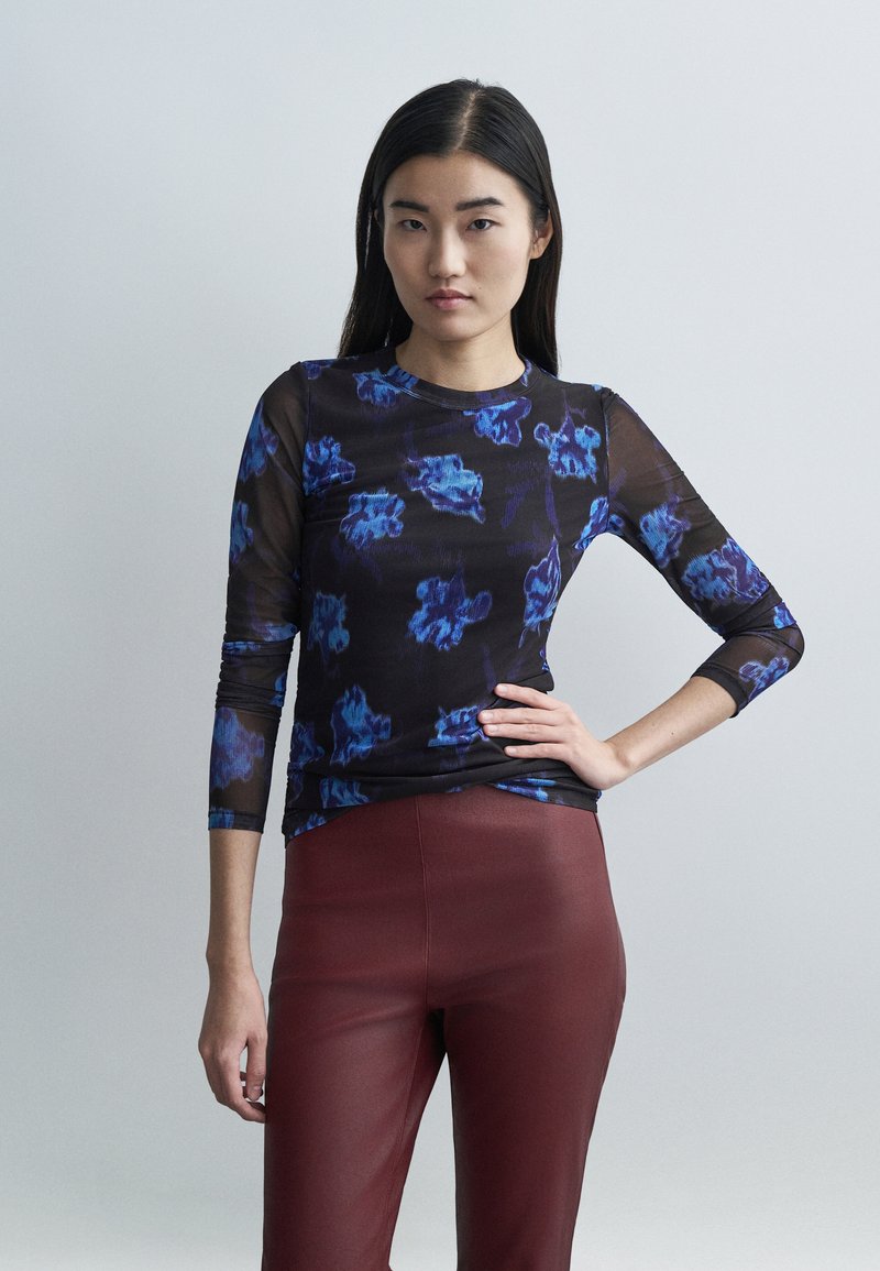 Langärmeliges schwarzes Mesh-Oberteil mit blauem Blumenmuster, rundem Ausschnitt und schmaler Passform. Kombiniert mit burgunderroten, eng geschnittenen Hosen.