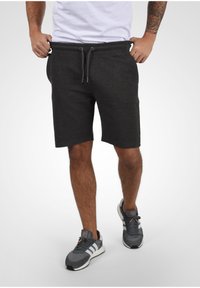 Shorts de sport gris foncé avec taille élastique, cordon de serrage et poches latérales. Associés à des baskets grises avec des rayures blanches.