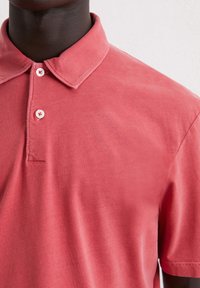 Licht koraalkleurig poloshirt van katoen, met een klassieke kraag, twee knopen en een gladde, licht gestructureerde afwerking.