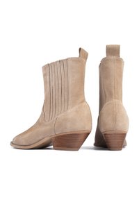 Botas de tobillo de ante beige con tacones de madera apilados, paneles laterales elásticos y tiradores en la parte trasera, mostradas desde ángulos laterales y traseros.