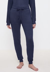 Mörkblå joggingbyxor i mjukt tyg, med dragsko i midjan, tapered cuffs och en slät yta. Inga mönster eller metalldelar.