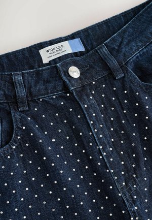 Wide leg, high-rise denim jeans in dark blue, featuring a dotted pattern of metallic studs, finished with a metallic button closure.
