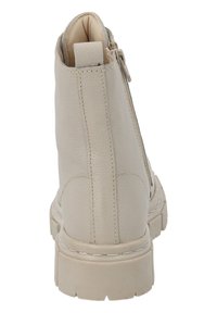Bottine en cuir beige avec une finition texturée, semelle épaisse et zip sur le côté. Présente des coutures contrastantes le long du bord et du talon.