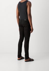 Czarny top na ramiączkach z wąskimi paskami, zestawiony z czarnymi, dopasowanymi jeansami z tylnymi kieszeniami. Noszony z czarnymi klapkami.