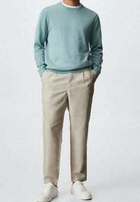 Lichtblauwe sweater, Beige geplooide broek en witte sneakers. Sweater heeft een ronde hals; broek is op maat gemaakt met zakken.