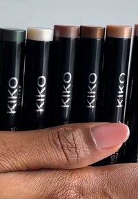 Kuuden KIKO Milano -meikkitikun setti esiteltynä kädessä, joissa on mattamustat putkilot nimet kaiverrettuna, ja eri ihonsävyisiä värejä kannen päällä.