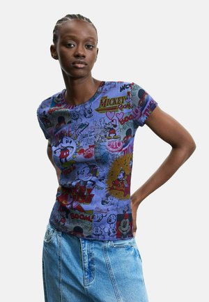 Ung kvinde iført en tætsiddende, kortærmet blå T-shirt med farverige vintage Mickey Mouse tegneserieprint og lyseblå cowboybukser.