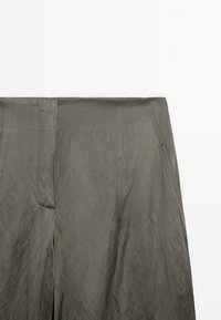 Pantalon taille haute couleur vert olive avec un tissu lisse et légèrement brillant, présentant des détails de coutures visibles à l'avant, sur un fond blanc.