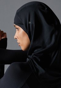 Svart atletisk hijab laget av teksturert, pustende stoff. Har en strømlinjeformet design med diskré logo-detalj, tilpasset rundt hodet og nakken.