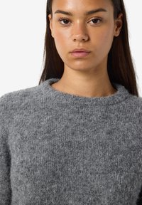 Grauer gestrickter Pullover mit weichem, strukturiertem Finish und Rundhalsausschnitt, der einen leicht lockeren Schnitt und gerippte Kanten aufweist.