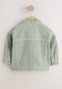 Veste en jean vert clair suspendue sur un cintre en bois, montrant le dos avec des poignets boutonnés et des détails cousus.