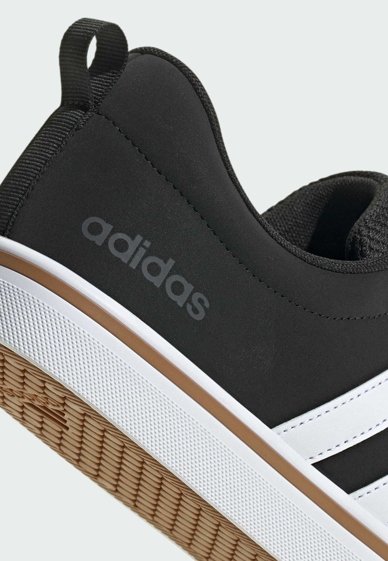 Schwarzer Sneaker mit glattem Gummiobermaterial, weißen Akzenten und einer texturierten Sohle. Verfügt über eine Schlaufe für leichteres Anziehen und das "adidas"-Logo in Grau.