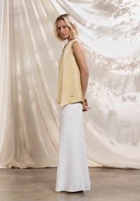 Haut jaune sans manches associé à une longue jupe blanche. Le haut a une coupe décontractée et la jupe est lisse avec un léger éclat.