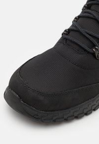 Zapatilla deportiva negra con un upper texturizado, diseño elegante y suela de goma con un agarre patrón. Costuras reforzadas a lo largo de los bordes.