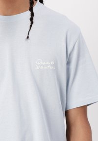 Light blue cotton t-shirt featuring a round neckline and short sleeves, with white embroidered text on the left chest that reads "Originals."