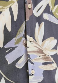 Tissu à motifs floraux en gris foncé avec de grandes feuilles blanches, beiges et olive. Comprend des boutons clairs le long de l'avant. Texture douce.