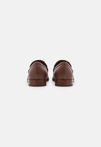 Mocassins en cuir marron avec des dos arrondis, une texture lisse, un minimalisme de couture et un talon en bois empilé. Design simple sans embellissements.