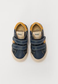 Sneakers din piele albă și galbenă cu două barete Velcro, talpă din cauciuc bej, cusături albe și interior căptușit.