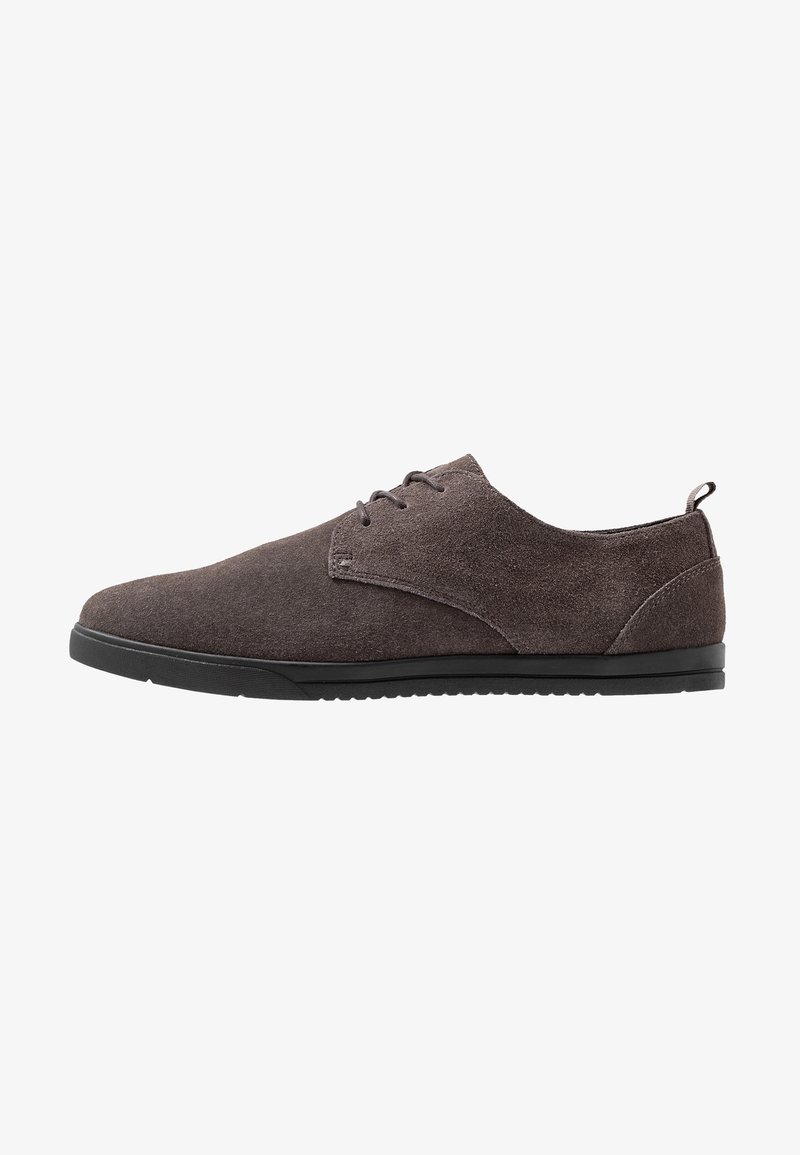Chaussure en daim marron à lacets avec semelle en caoutchouc noir et petit talon, vue de profil sur fond blanc.